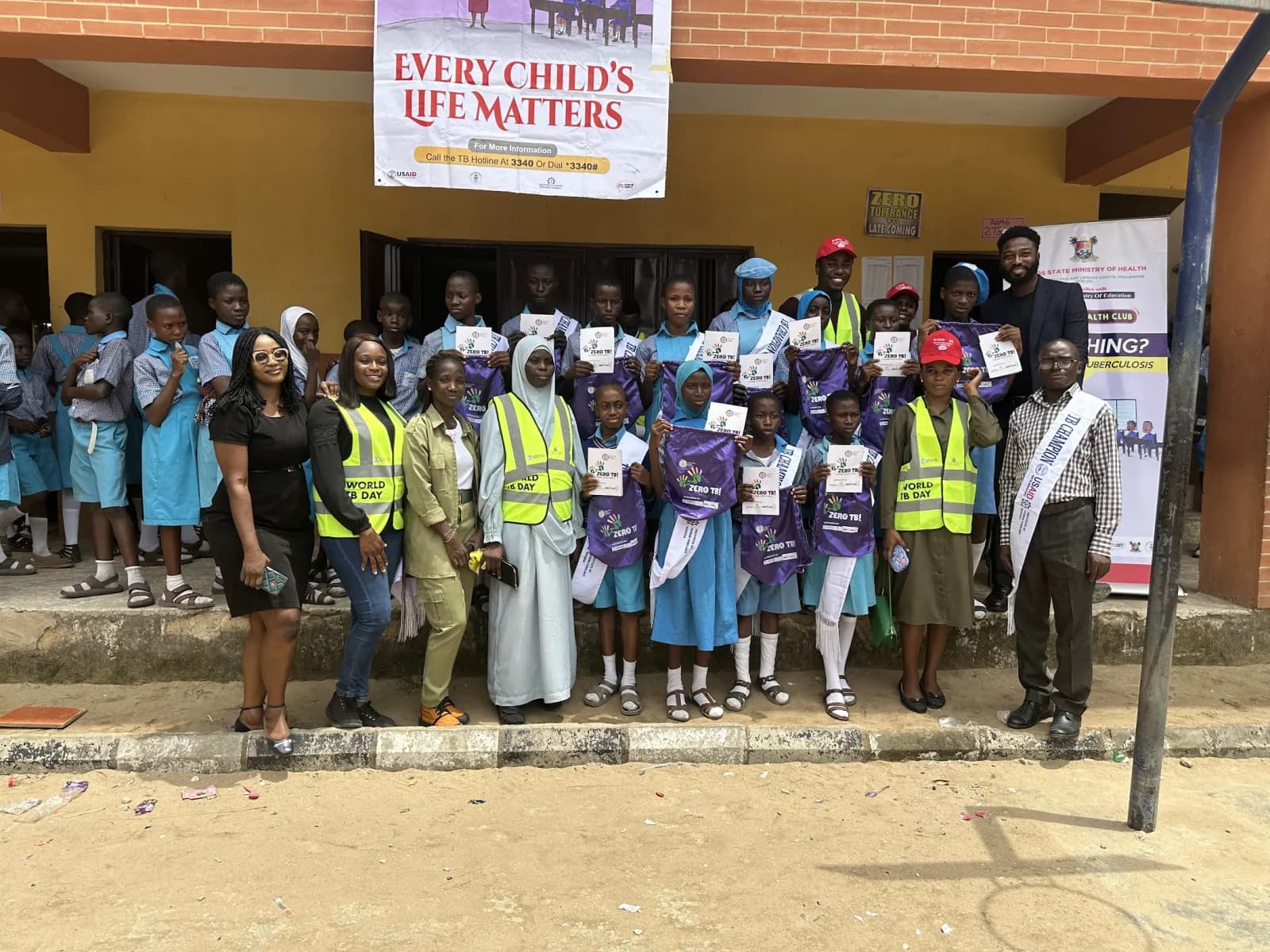 Volunteers and pupils holding Zero TB materials outside a Lagos school on World TB Day